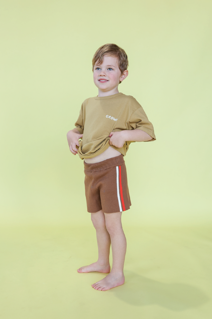 Young boy wearing a mustard t-shirt and brown shorts on a yellow background