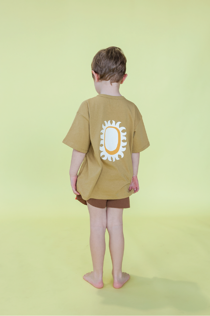 Young boy wearing a mustard t-shirt and brown shorts on a yellow background