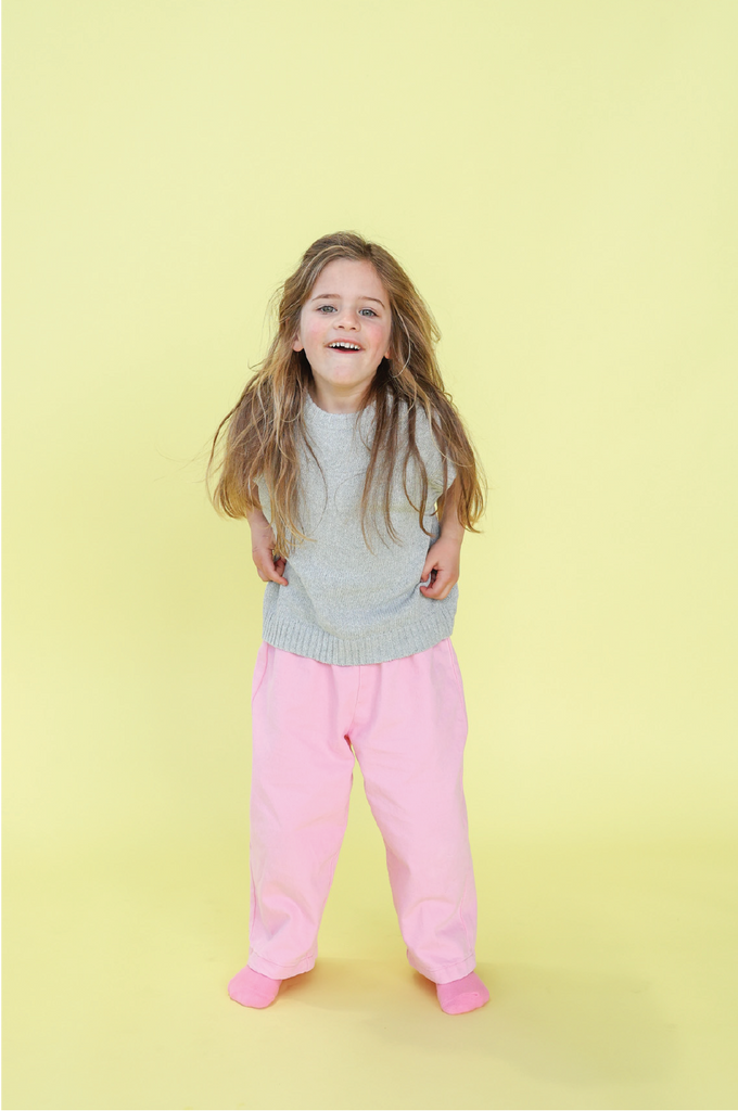Young girl wearing a grey knit vest and pink denim jeans on a yellow background