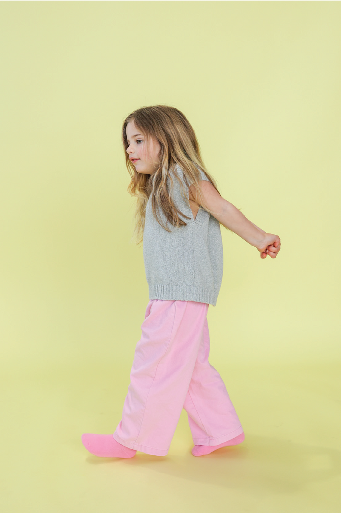 Young girl wearing a grey knit vest and pink denim jeans on a yellow background
