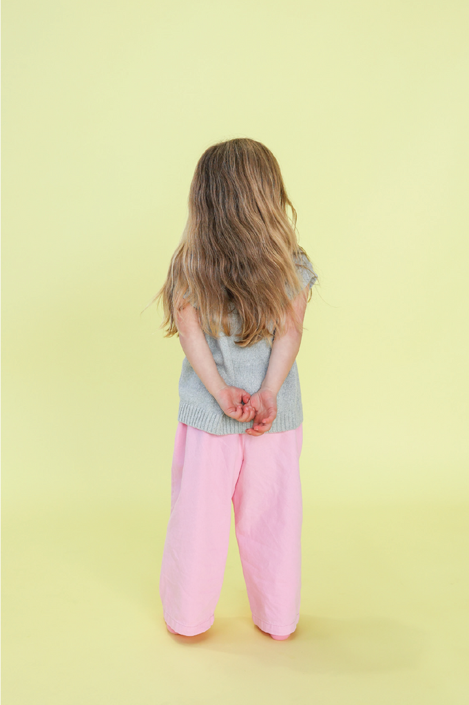 Young girl wearing a grey knit vest and pink denim jeans on a yellow background