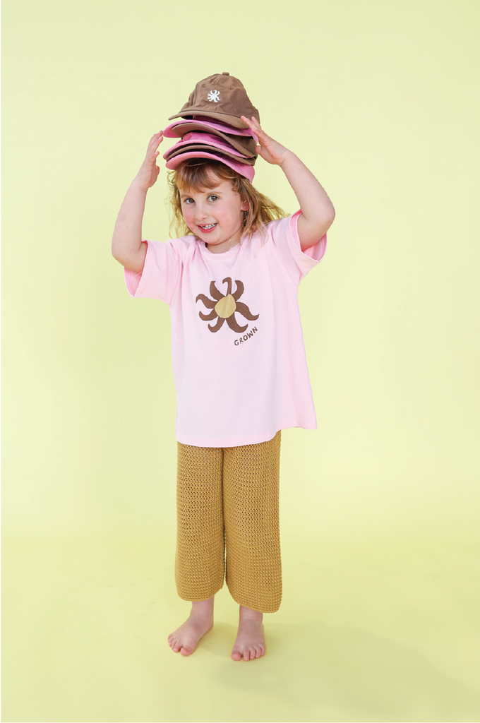 Young girl wearing a pink t-shirt with a sun design and mustard knit pants on a yellow background