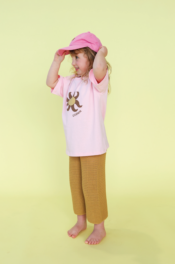 Young girl wearing a pink t-shirt with a sun design and mustard knit pants on a yellow background