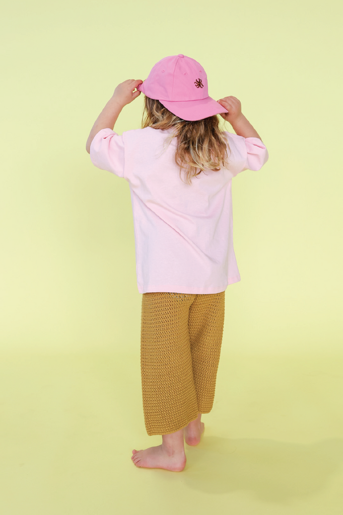 Young girl wearing a pink t-shirt with a sun design and mustard knit pants on a yellow background