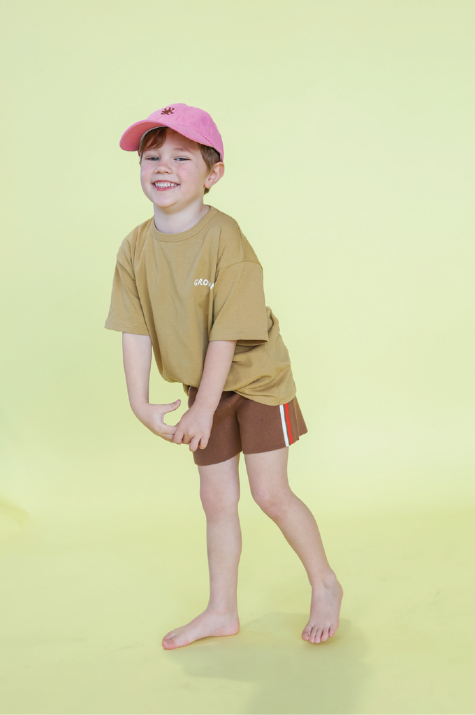 Young boy wearing a mustard t-shirt and brown shorts on a yellow background