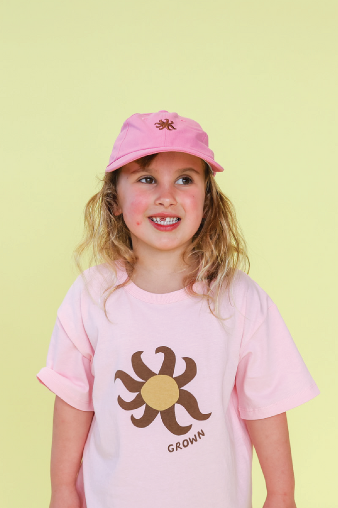 Child wearing a pink cap with a logo on a yellow background