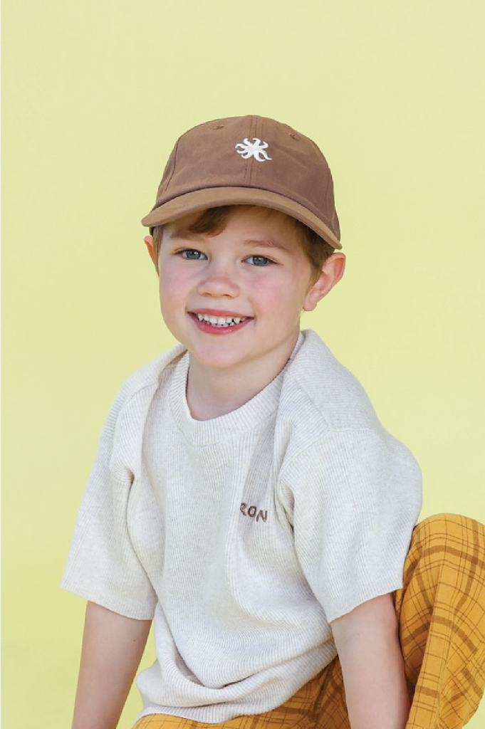 Child wearing a brown cap and white shirt with a yellow background