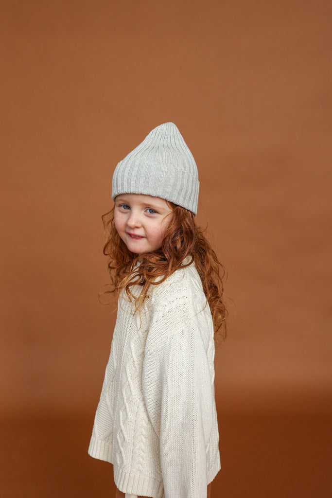 close up White milk sweater with cable knit pattern made from organic cotton for children with grey knitted beanie and brown knitted pants
