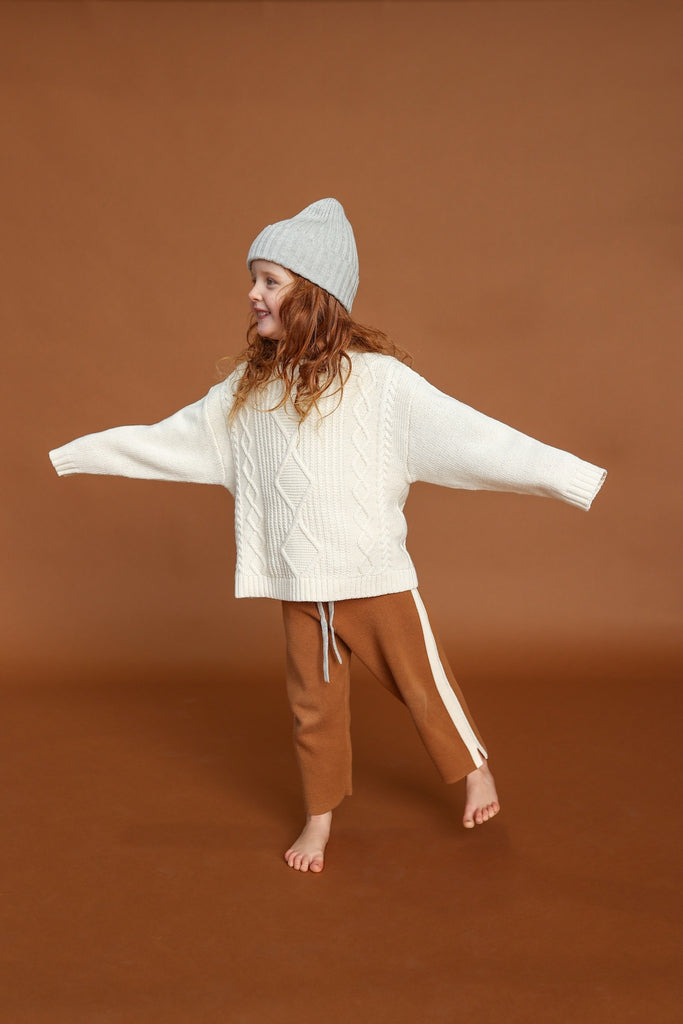 White milk sweater with cable knit pattern made from organic cotton for children with grey knitted beanie and brown knitted pants