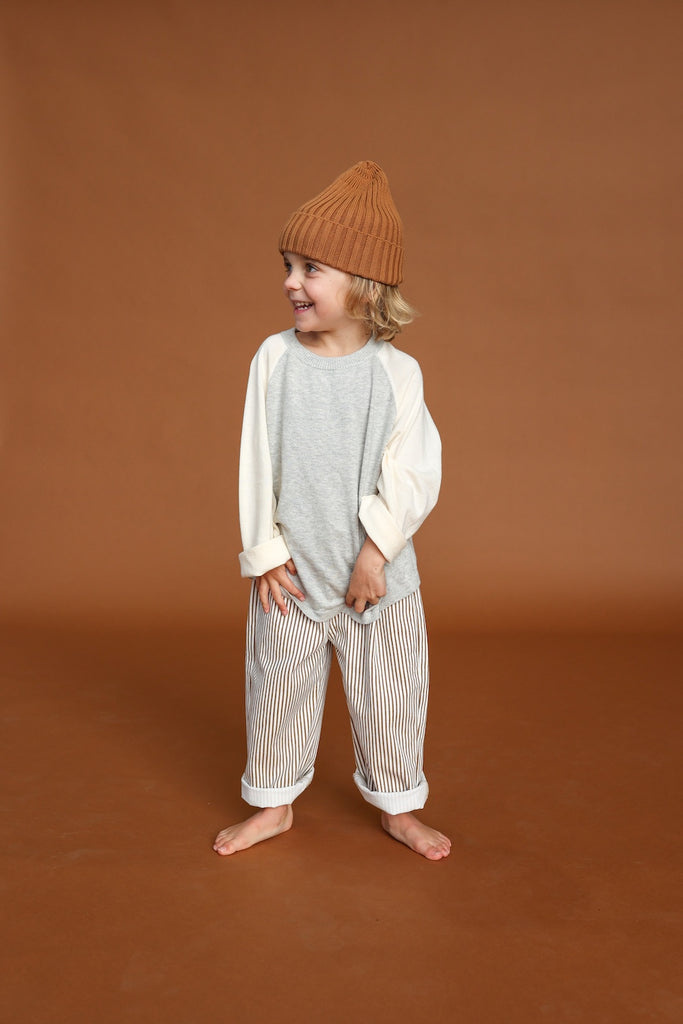 Child wearing a brown beanie and striped pants on a brown background