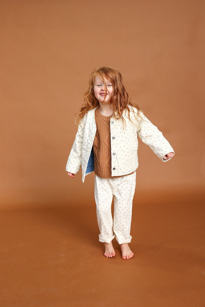 Child wearing a white jacket and brown shirt on a brown background