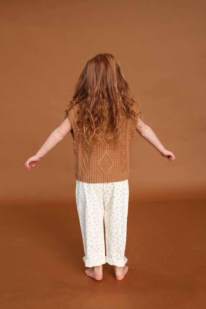 Child wearing a brown knitted top and white floral pants on a brown background