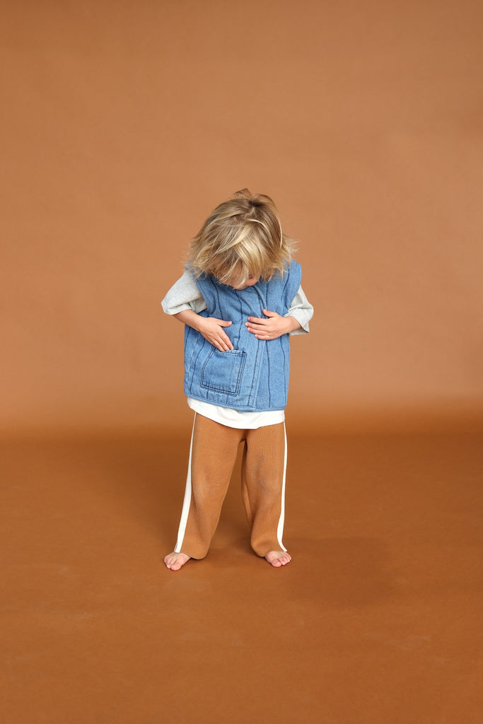 Child wearing a blue vest and brown pants on a brown background