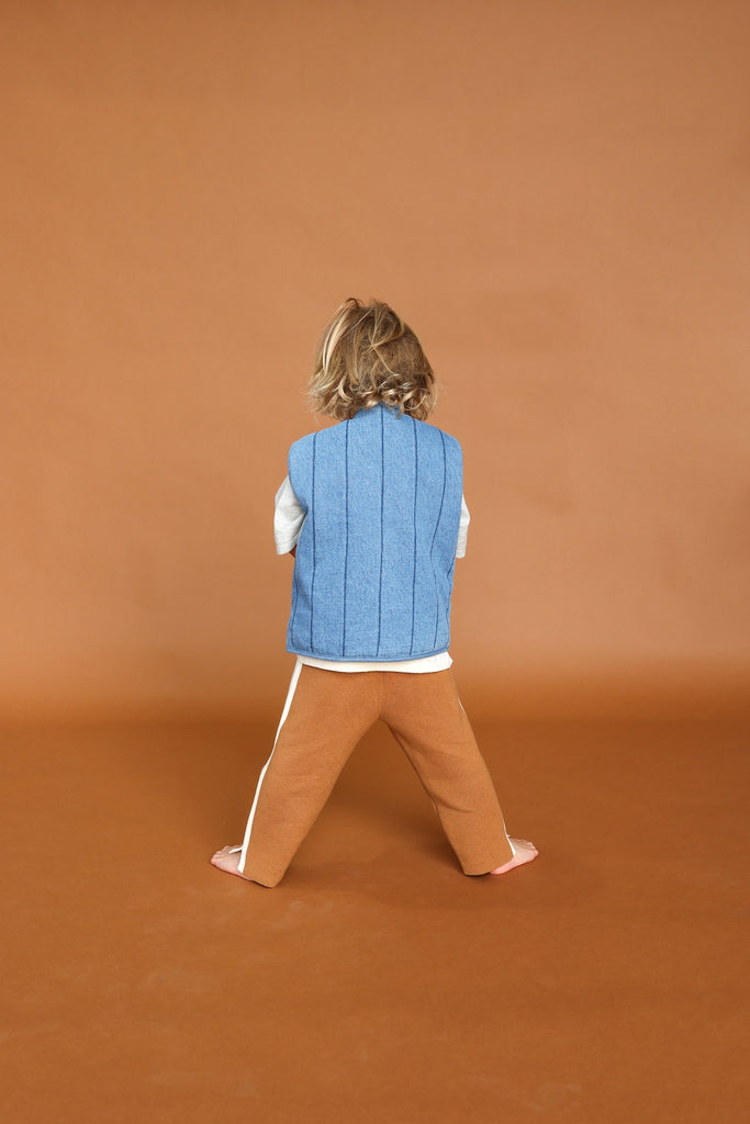 Child wearing a blue vest and brown pants against a brown background