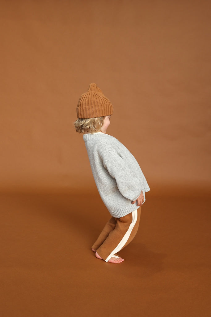 Child wearing a gray sweater and brown pants on a brown background