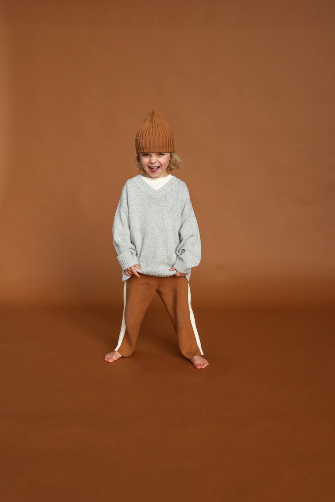 Child wearing a gray sweater and brown pants on a brown background