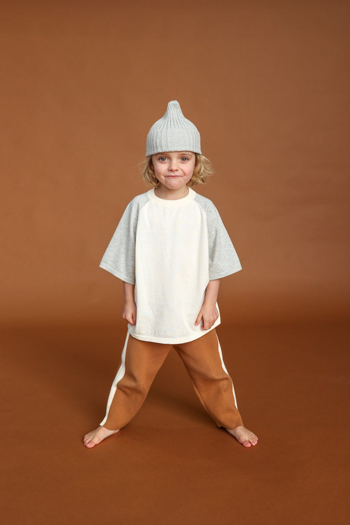 Child wearing a light gray knit hat and a neutral coloured outfit on a brown background